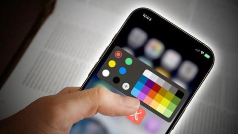 من iPhoneIslam.com، يد تحمل هاتفًا ذكيًا تعرض أداة لوحة الألوان على الشاشة، مع أيقونات تطبيقات غير واضحة في الخلفية، تذكرنا بواجهات العرض المبتكرة في مؤتمر المطورين العالمي.