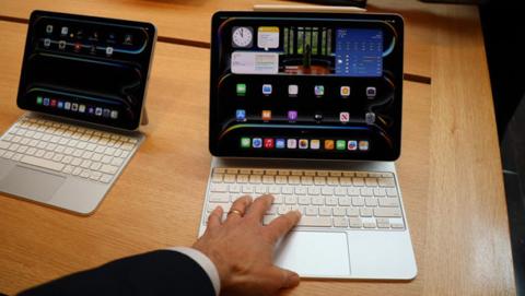 من iPhoneIslam.com، يتفاعل الشخص مع جهاز آي باد برو المتصل بلوحة المفاتيح على طاولة خشبية. يتم عرض جهاز آخر مماثل في الخلفية.