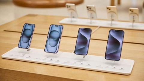 من iPhoneIslam.com، يتم عرض أربعة هواتف ذكية في أحد متاجر البيع بالتجزئة، ويظهر كل منها شاشة ملونة مختلفة. يوجد في الخلفية المزيد من الهواتف على حامل منفصل. الهامشصفقات استثنائية متوقعة في شهر مايو.