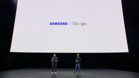 من iPhoneIslam.com، رجلان يقفان على خشبة المسرح ويحملان شعار سامسونج في حدث مؤتمر Unpacked 2024.